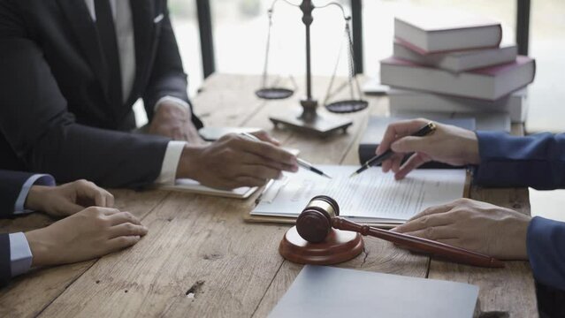 Multiethnic lawyers working with documents and discussing at conference table in law office, justice concept with scales and hammer on table