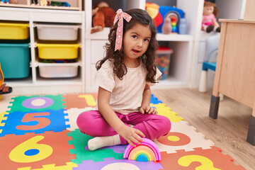 Adorable hispanic girl playing with construction blocks sitting on floor at kindergarten