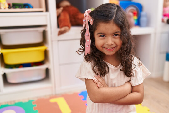 Adorable hispanic girl smiling confident sitting on floor with arms crossed gesture at kindergarten
