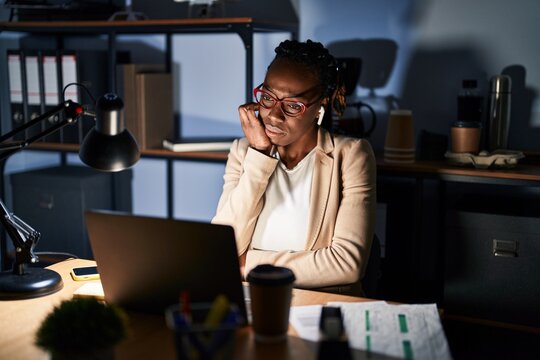 Beautiful black woman working at the office at night looking stressed and nervous with hands on mouth biting nails. anxiety problem.