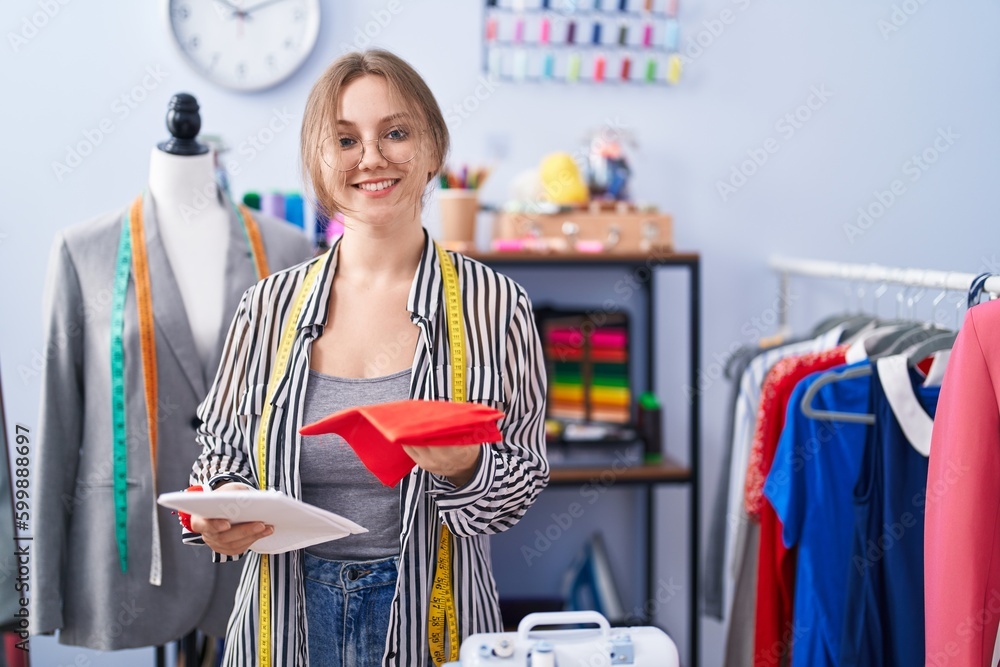 Wall mural Young blonde woman tailor smiling confident holding cloths at tailor shop