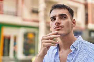 Young hispanic man standing with doubt expression at street