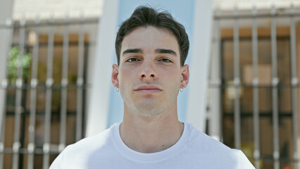 Young hispanic man standing with serious expression at street