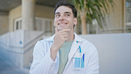 Young hispanic man doctor smiling confident thinking at hospital