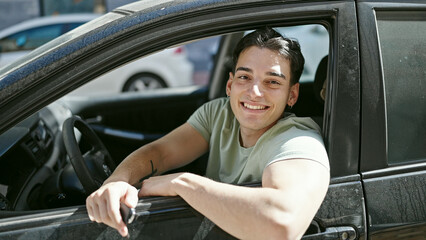 Obraz premium Young hispanic man smiling confident sitting on car at street