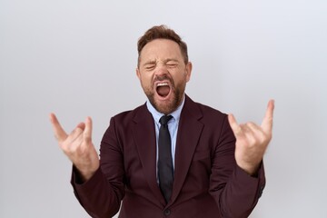 Middle age business man with beard wearing suit and tie shouting with crazy expression doing rock symbol with hands up. music star. heavy music concept.