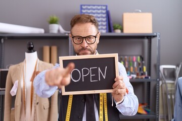 Middle age man with beard dressmaker designer holding open sign pointing with finger to the camera and to you, confident gesture looking serious