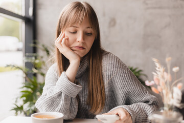 Single sad girl waiting for a phone call sitting in a table in restaurant. Blonde woman with bang...