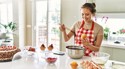 Young beautiful hispanic woman smiling confident putting chocolate on muffin at the kitchen