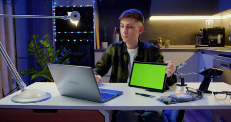 Attractive boy using laptop working have call video conference. Teenager shows tablet with green...