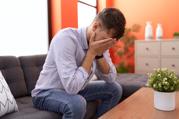 Young hispanic man stressed sitting on sofa at home