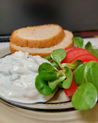 Serek ziołowy z pieczywem, pomidorem i roszpunką / Herbed cheese with bread, tomato, and arugula.