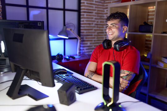 Young hispanic man streamer smiling confident sitting with arms crossed gesture at gaming room