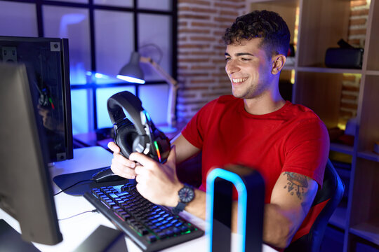 Young hispanic man streamer smiling confident holding headphones at gaming room