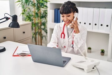 Young woman wearing doctor uniform talking on the telephone at clinic