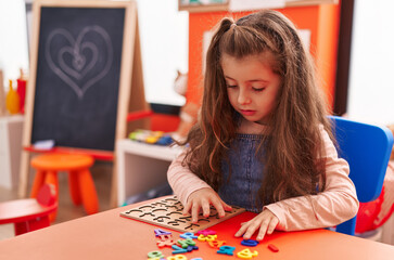 Fototapeta premium Adorable hispanic girl playing with maths puzzle game sitting on table at kindergarten
