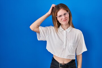 Beautiful woman standing over blue background confuse and wonder about question. uncertain with doubt, thinking with hand on head. pensive concept.