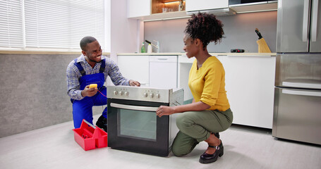 Smiling Repairman Repairing Oven On Kitchen Worktop In Front