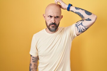Hispanic man with tattoos standing over yellow background confuse and wondering about question....