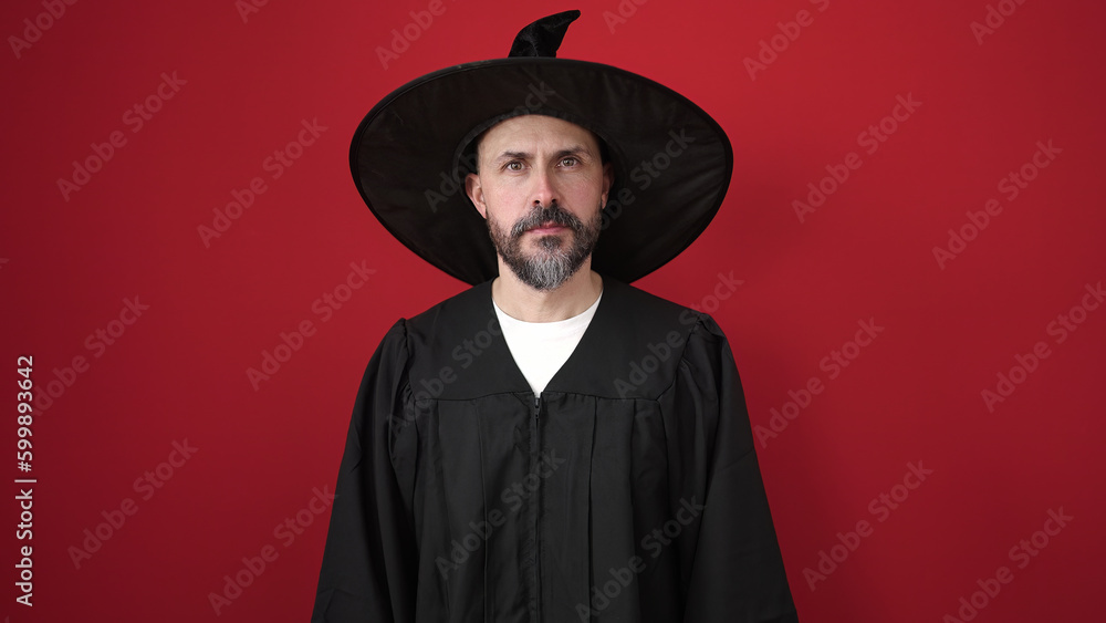 Sticker Young bald man wearing wizard costume standing over isolated red background