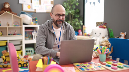 Young bald man preschool teacher using laptop working at kindergarten
