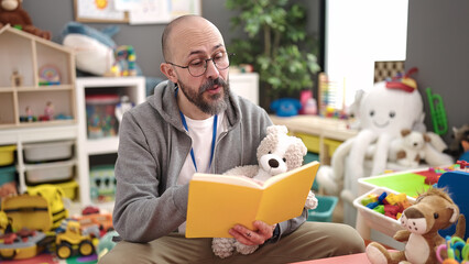 Young bald man preschool teacher reading story book at kindergarten