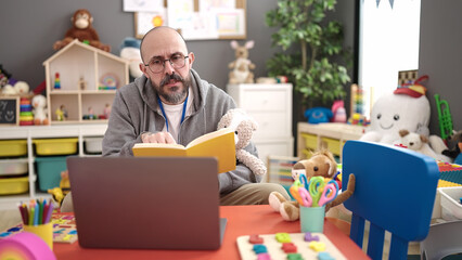 Young bald man preschool teacher reading story book on a video call at kindergarten