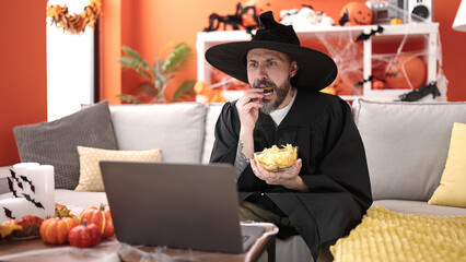 Young bald man wearing wizard costume eating chips potatoes watching movie at home