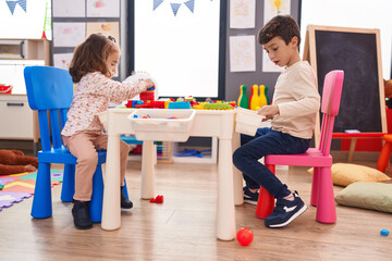 Adorable boy and girl playing with construction blocks sitting on table at kindergarten