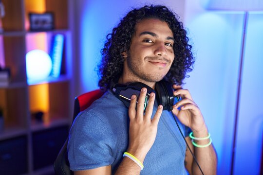 Young latin man streamer smiling confident sitting on table at gaming room