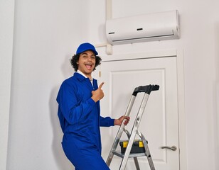 Hispanic man with curly hair working at home renovation smiling happy pointing with hand and finger