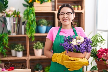 Hispanic young woman working at florist shop holding plant winking looking at the camera with sexy...