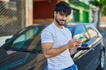 Fototapeta na wymiar Young hispanic man using smartphone leaning on car at street