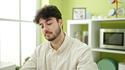 Young hispanic man sitting on table with relaxed expression at dinning room