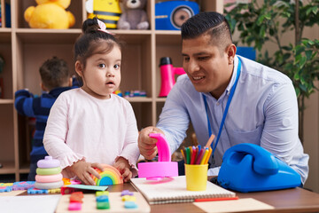 Hispanic man with boy and girl playing with construction blocks sitting on table at kindergarten