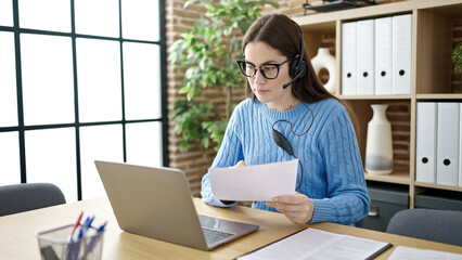 Young caucasian woman call center agent reading document working at office