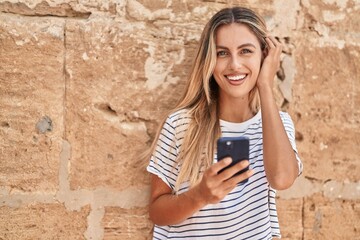 Young blonde woman smiling confident using smartphone over isolated stone background