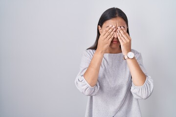 Young hispanic woman standing over white background rubbing eyes for fatigue and headache, sleepy...