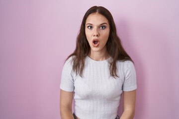 Fototapeta premium Young hispanic girl standing over pink background afraid and shocked with surprise and amazed expression, fear and excited face.