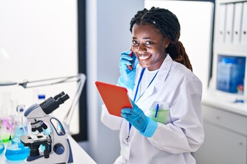 African american woman scientist talking on smartphone using touchpad at laboratory
