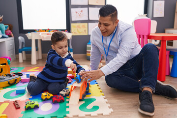 Hispanic man and boy playing with car toy sitting on floor at kindergarten