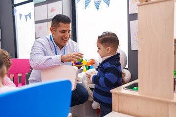 Obraz premium Hispanic man and boy playing with play kitchen standing at kindergarten