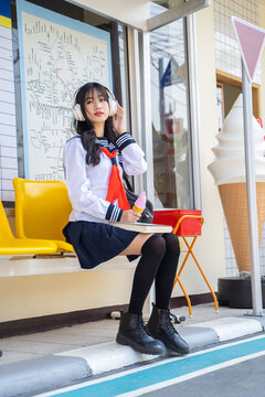 Portrait of a happy japanese school girl listening to music via headphones at ice cream shop, Japanese female students, girl student in school uniform japanese style