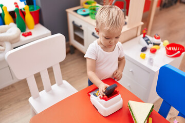 Adorable caucasian boy holding sandwich and supermarket toy at kindergarten