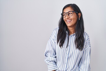 Young hispanic woman wearing glasses looking away to side with smile on face, natural expression....