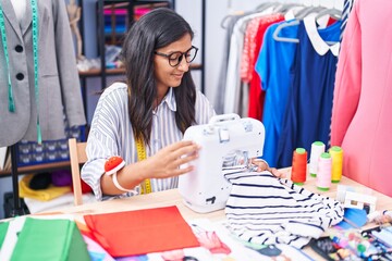 Fototapeta premium Young beautiful hispanic woman tailor smiling confident using sewing machine at clothing factory