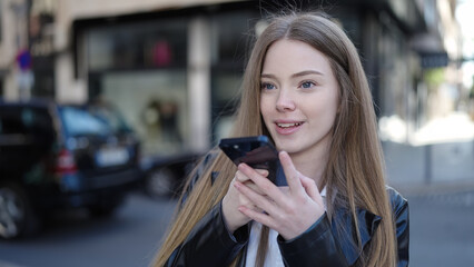 Young blonde woman sending voice message with smartphone at street