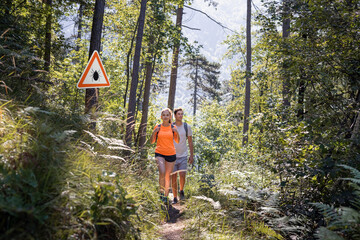 Man and woman hiking in Infected ticks forest with warning sign. Risk of tick-borne and lyme...