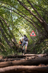 Man and woman hiking in Infected ticks forest with warning sign. Risk of tick-borne and lyme...