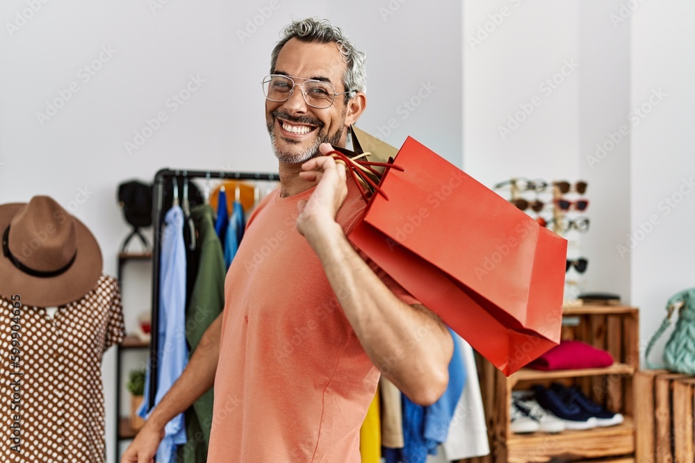 Wall mural Middle age grey-haired man customer smiling confident holding shopping bags at clothing store